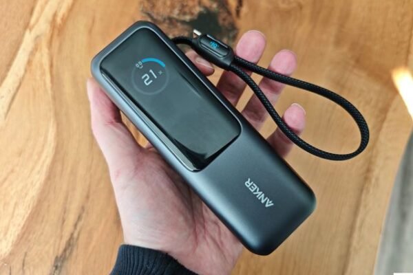 A hand holding an Anker Laptop Power Bank, a black rectangular portable charger with long digital screen.