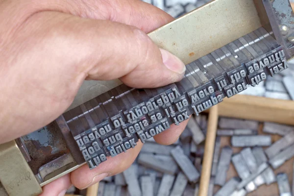 Closeup photo of a hand holding a metal type template for lettering.