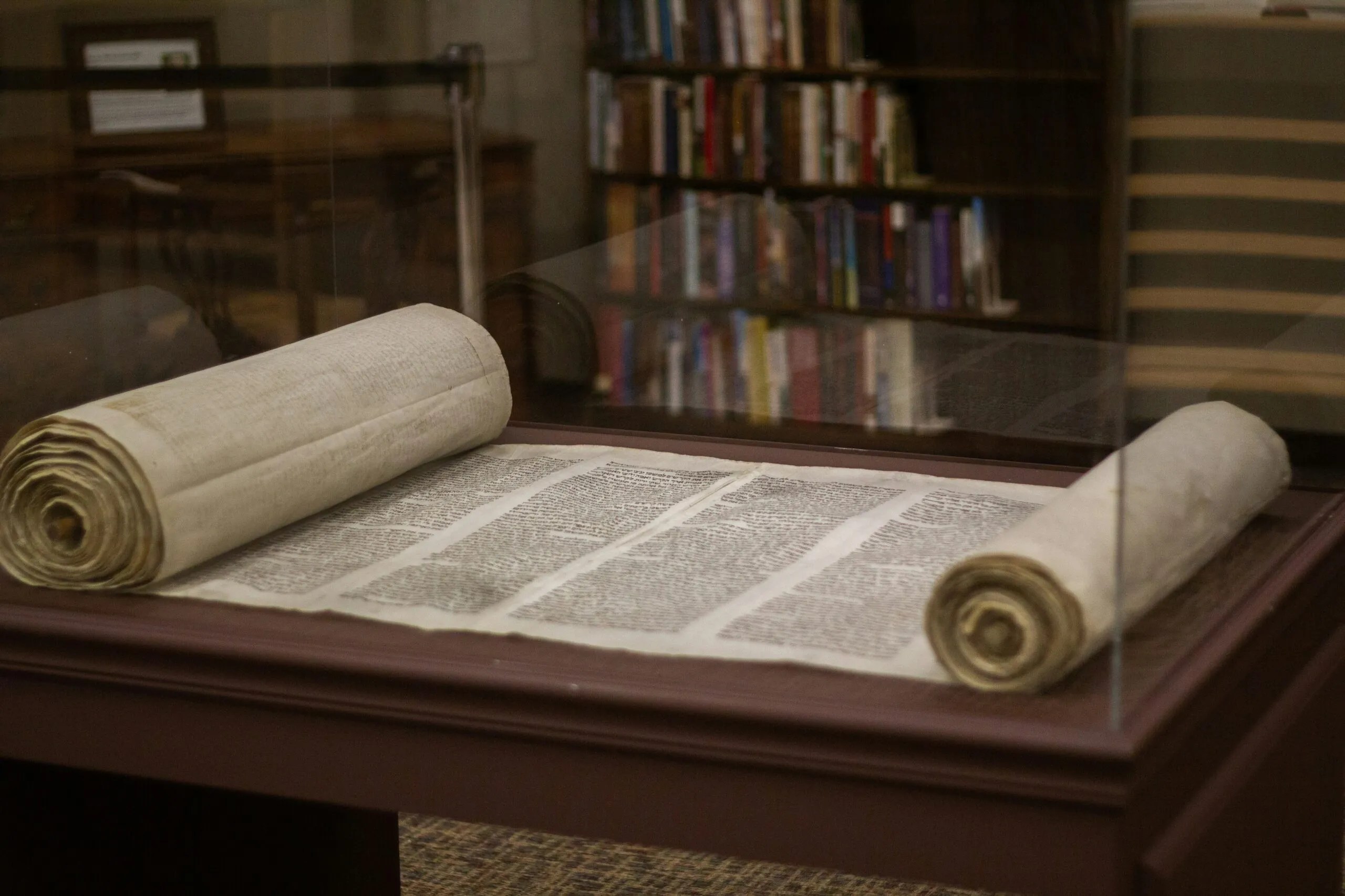 Photo of an ancient scroll partially unrolled inside a glass case on a wooden desk.